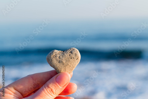 female hand holds a heart of natural stone against the background of the sea in the sun. Reminder of mother's day, valentine's day, stone wedding, etc.