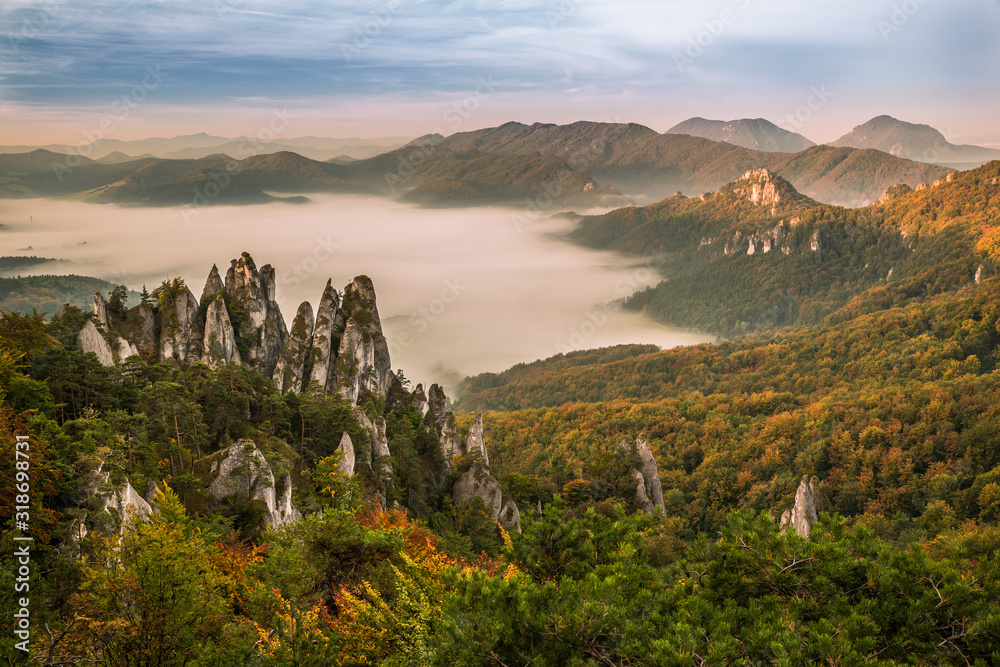 The morning mist enveloped the landscape under the mountains, illuminated by the rising sun. Bizarre rocks formations in autumn colors.