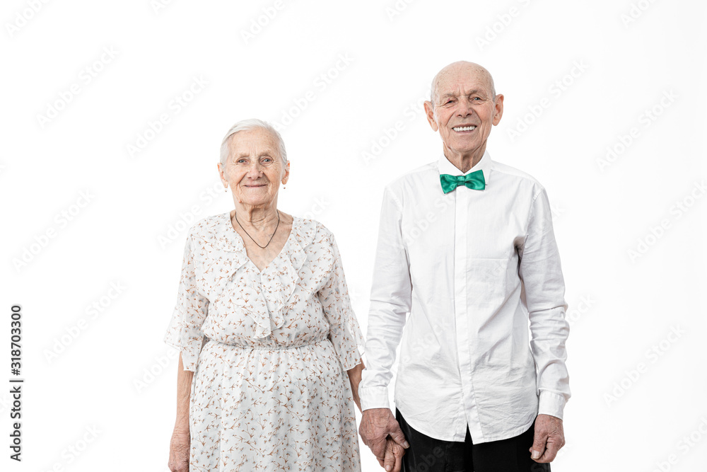 Portrait of happy, smiling, romantic senior man with his wife, old woman in white dress and old man in white shirt holding hands together and looking at the camera, isolated over white background Portrait of happy, smiling, romantic senior man with his wife, old woman in white dress and old man in white shirt holding hands together and looking at the camera, isolated over white background