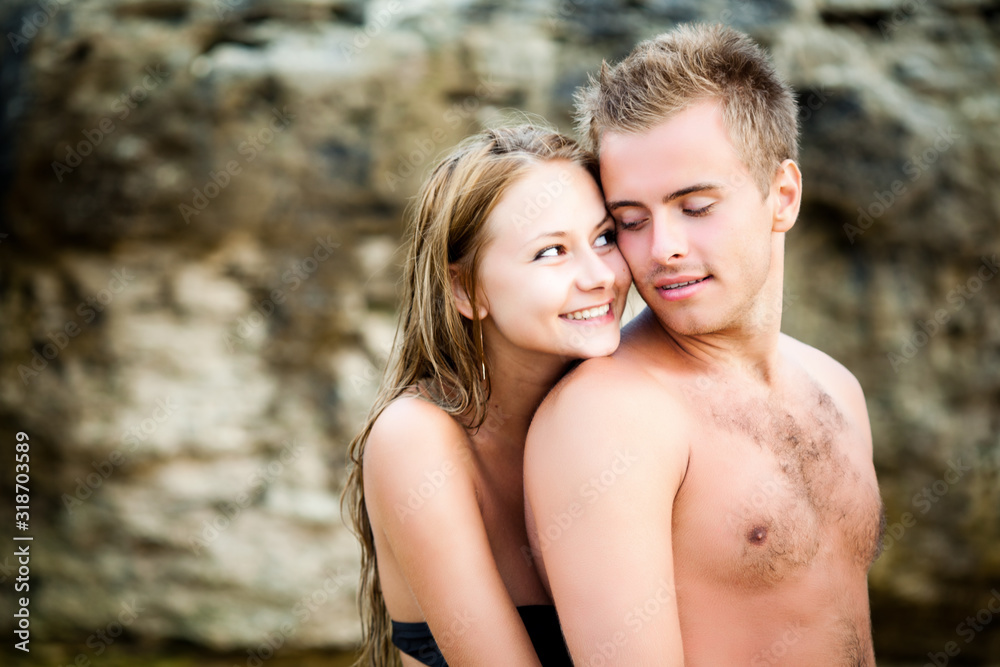 Young beautiful smiling woman embracing from back her happy boyfriend with natural rocks at background on clear summer day. Travelling, vacations, romantic weekend, honeymoon concept Young beautiful smiling woman embracing from back her happy boyfriend with natural rocks at background on clear summer day. Travelling, vacations, romantic weekend, honeymoon concept