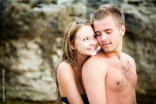 Young beautiful smiling woman embracing from back her happy boyfriend with natural rocks at background on clear summer day. Travelling, vacations, romantic weekend, honeymoon concept
