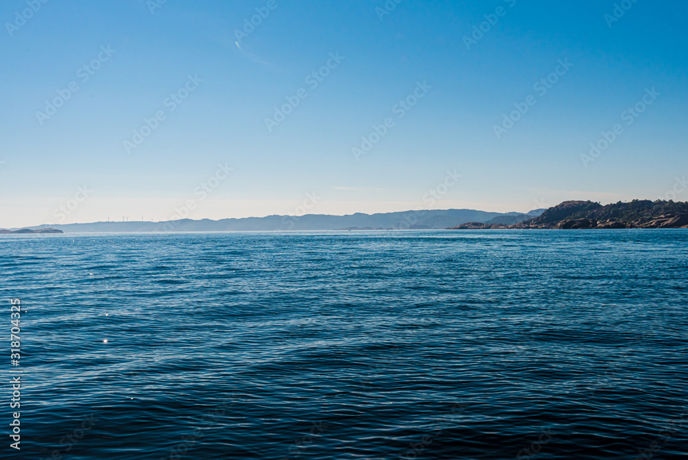 Obraz premium View over small waves at sea with land in the horizon.