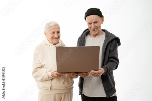 Couple of stylish seniors in casual clothes smiling and looking at the same laptop hugged isolated over white background - indoor, at home concept - european mature and retired man and woman using