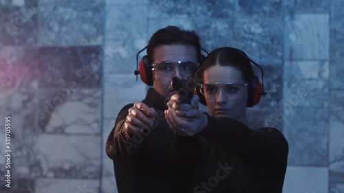 A man teaches a woman how to shoot a gun indoors pistol speed firing girl police practice target training young away distance electric female flash detective close up slow motion