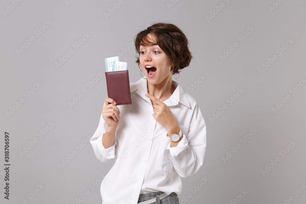 Excited young business woman in white shirt posing isolated on grey background. Achievement career wealth business concept. Mock up copy space. Pointing index finger on passport boarding pass, ticket. Excited young business woman in white shirt posing isolated on grey background. Achievement career wealth business concept. Mock up copy space. Pointing index finger on passport boarding pass, ticket.