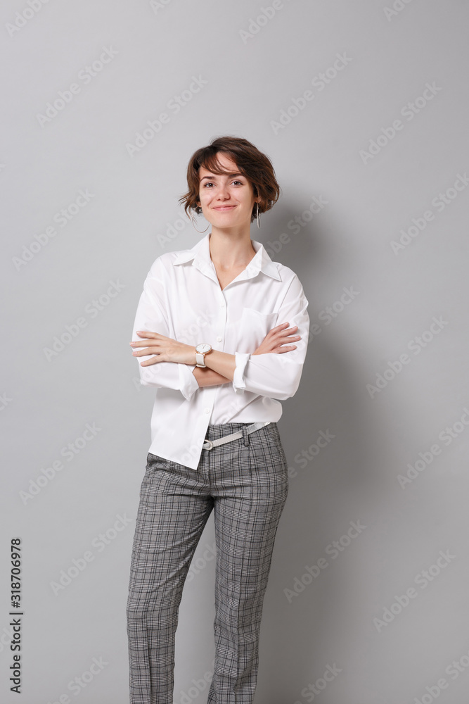 Smiling beautiful young business woman in white shirt posing isolated on grey wall background studio portrait. Achievement career wealth business concept. Mock up copy space. Holding hands crossed. Smiling beautiful young business woman in white shirt posing isolated on grey wall background studio portrait. Achievement career wealth business concept. Mock up copy space. Holding hands crossed.