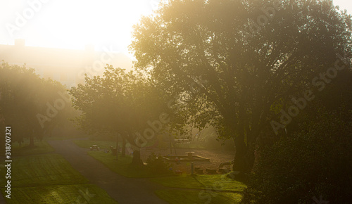 The sun shining throug dense morning fog over a playground.