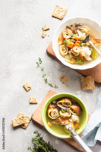 Vegetable soup with egg pancakes on light grey background. Traditional German Flaedlesuppe and Austrian Frittatensuppe.  photo