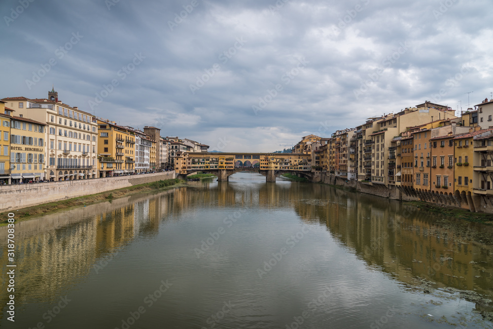 Ponte Vecchio in historical center downtown in Florence during sunrise with water reflections in Arno river