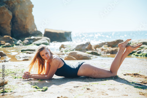 young blonde girl in a black bathing suit lies on the beach. sea holiday