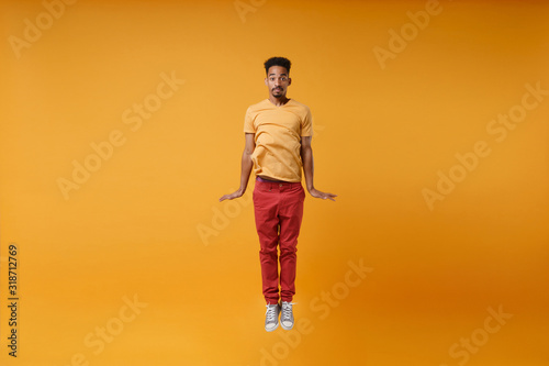 Funny young african american guy in bright casual clothes posing isolated on yellow orange wall background, studio portrait. People sincere emotions lifestyle concept. Mock up copy space. Jumping.