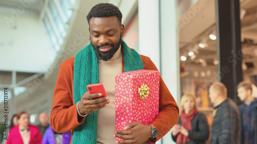 In shop mall african american young man use phone walk Christmas time background Christmas tree feel happy shopping internet face close up portrait mobile technology close up slow motion