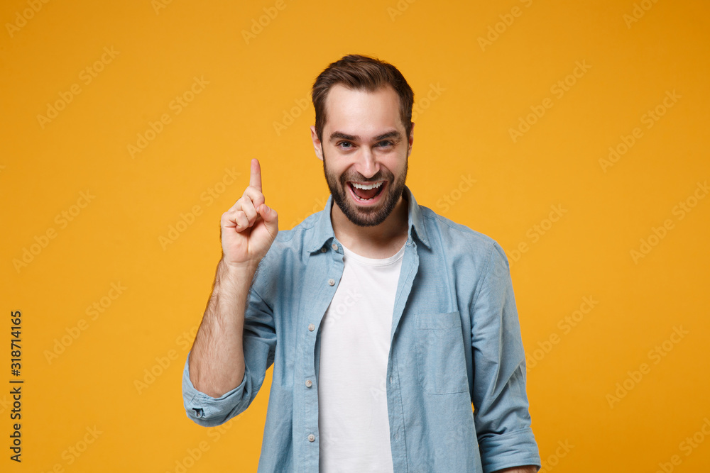 Excited young bearded man in casual blue shirt posing isolated on yellow orange background studio portrait. People lifestyle concept. Mock up copy space. Holding index finger up with great new idea. Excited young bearded man in casual blue shirt posing isolated on yellow orange background studio portrait. People lifestyle concept. Mock up copy space. Holding index finger up with great new idea.
