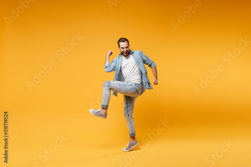 Joyful young bearded man in casual blue shirt posing isolated on yellow orange background studio portrait. People sincere emotions lifestyle concept. Mock up copy space. Clenching fists like winner.