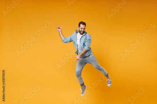 Funny young bearded man in casual blue shirt posing isolated on yellow orange wall background studio portrait. People lifestyle concept. Mock up copy space. Jumping fooling around like playing guitar.
