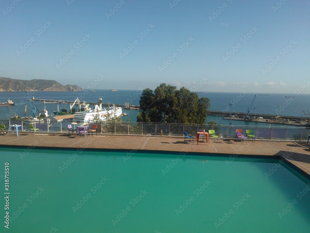wonderful view with, swimming pool, blue sea, harbor and chairs under the sun