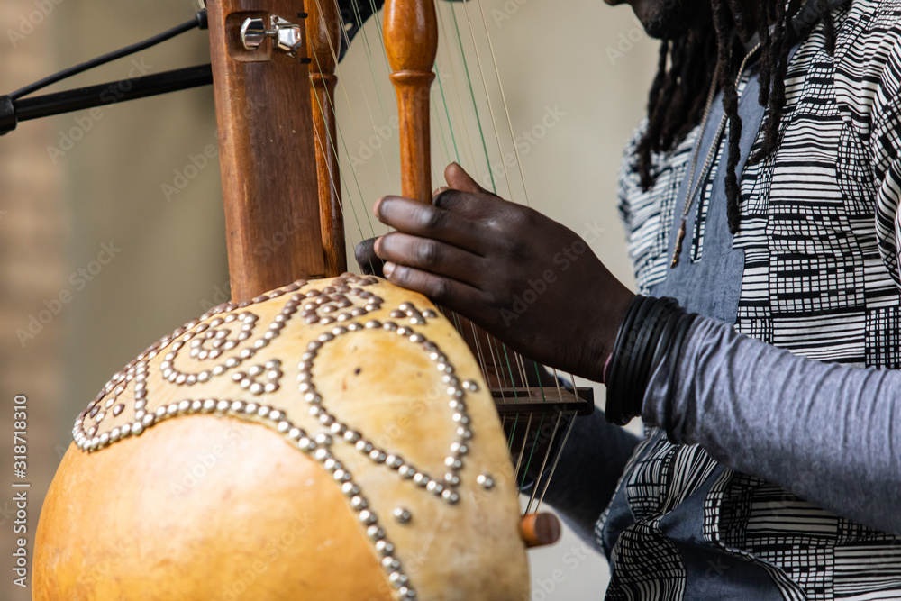Naklejka premium Midsection of male artist with dreadlocks wearing bracelets while performing traditional wooden harp kora during event with focus on foreground