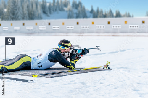 Biathlete lies and shoots a target at a 20 km race. Athlete with modern sports equipment for competition photo