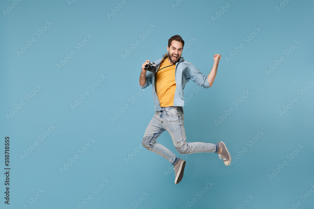 Happy traveler tourist man in yellow summer clothes with photo camera isolated on blue background. Male passenger traveling abroad on weekend. Air flight journey concept. Jumping doing winner gesture. Happy traveler tourist man in yellow summer clothes with photo camera isolated on blue background. Male passenger traveling abroad on weekend. Air flight journey concept. Jumping doing winner gesture.