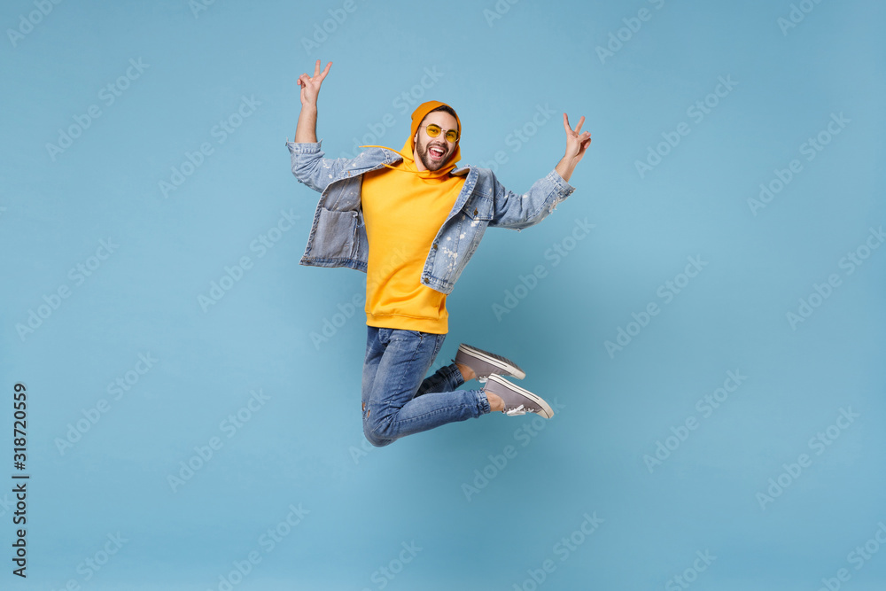Cheerful young hipster guy in fashion jeans denim clothes posing isolated on pastel blue background in studio. People lifestyle concept. Mock up copy space. Jumping, screaming, showing victory sign. Cheerful young hipster guy in fashion jeans denim clothes posing isolated on pastel blue background in studio. People lifestyle concept. Mock up copy space. Jumping, screaming, showing victory sign.