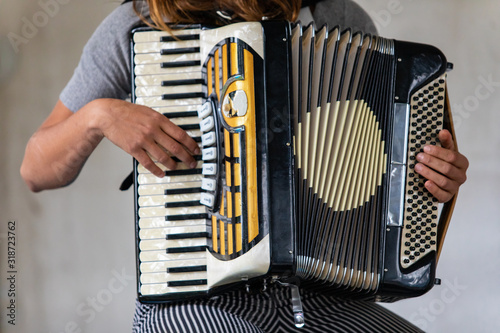 Closeup midsection of female artist wearing gray t-shirt and stripped pant while playing classical accordion and sitting against wall