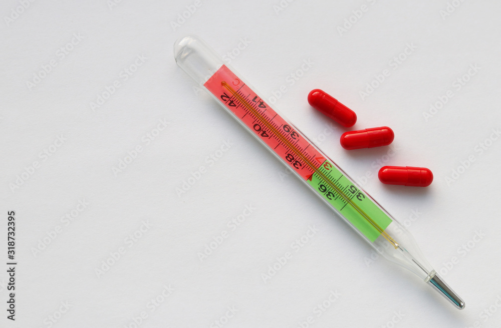 Glass thermometer and three red capsules on a white background. Selective focus. Copy space. Medical supplies and medicines. Treatment and health care Glass thermometer and three red capsules on a white background. Selective focus. Copy space. Medical supplies and medicines. Treatment and health care