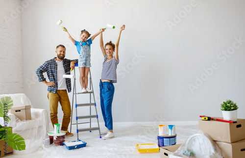 Fototapeta Naklejka Na Ścianę i Meble -  Repair in apartment. Happy family mother, father and child daughter  paints wall .