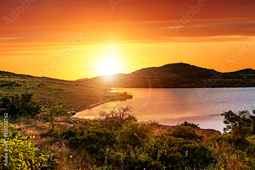 Fototapeta Naklejka Na Ścianę i Meble -  A bright orange crimson sunset in the valley of Wichita Mountains Wildlife Refuge near Lawton, Oklahoma, USA.