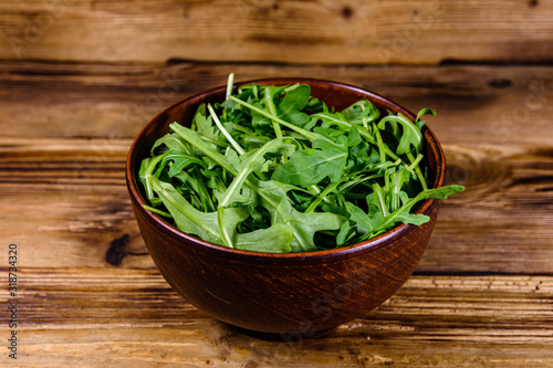 Ceramic bowl with arugula leaves on wooden table
