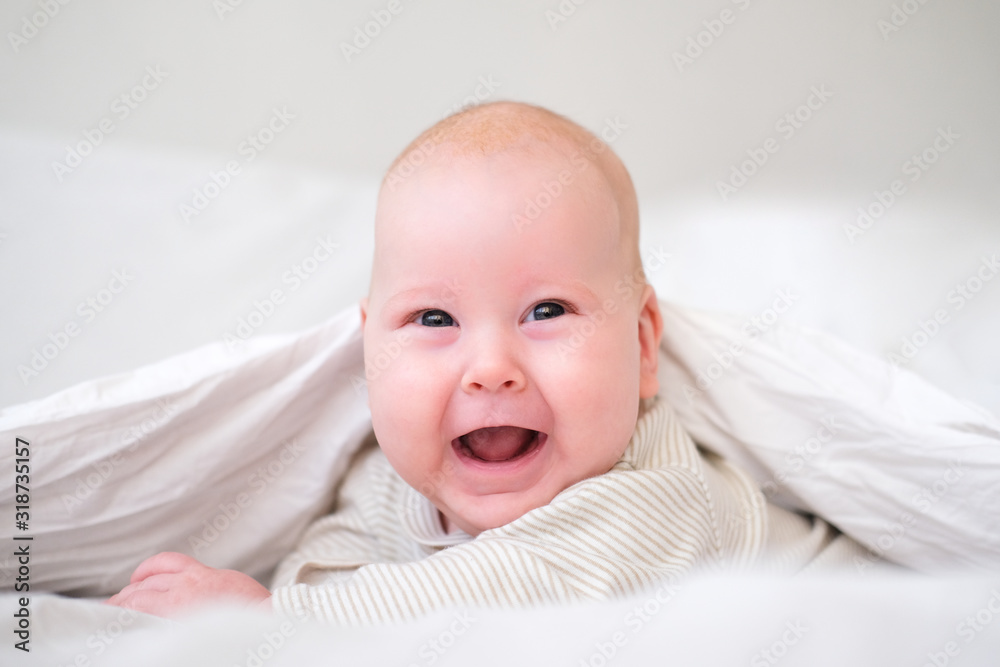 Adorable smiling baby boy under white blanket in bedroom. Newborn child relaxing in bed. Family morning at home. New born infant kids. Adorable smiling baby boy under white blanket in bedroom. Newborn child relaxing in bed. Family morning at home. New born infant kids.