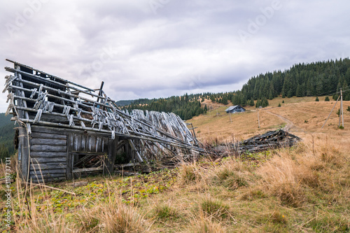 Stack of wooden planks of old shed up in mountains with cloudy sky and dried grass around.