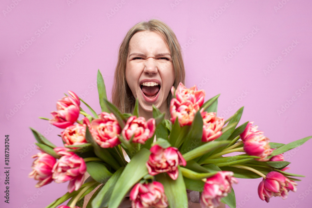 emotional girl holds a bouquet of flowers on a pink background, a happy woman with tulips screams for joy