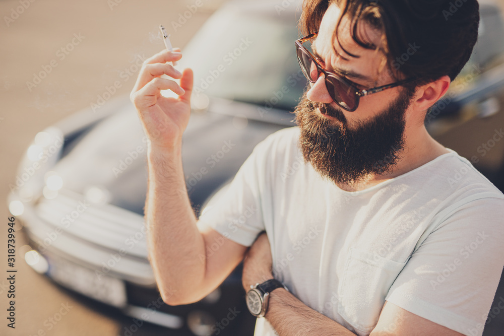 Hipster smoking cigarette near car