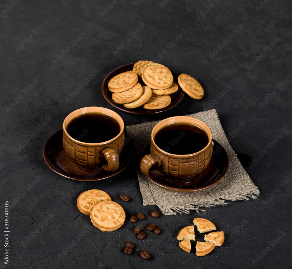 Fototapeta premium Round shortbread cookies in the shape of coins and a Cup of black coffee on a dark gray background in rustic style