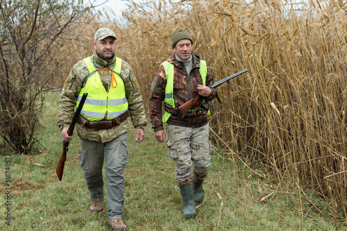 Hunting period, autumn season open. A hunter with a gun in his hands in hunting clothes in the autumn forest in search of a trophy. A man stands with weapons and hunting dogs tracking down the game...