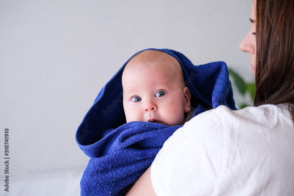 Mom hugs her little cutest baby after bath with blue towel on head. Infant child on mother hands. Mothercare love. Family life. Mother and baby. Happy motherhood. Mom hugs her little cutest baby after bath with blue towel on head. Infant child on mother hands. Mothercare love. Family life. Mother and baby. Happy motherhood.