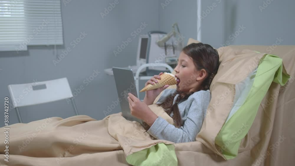 Girl lie on the bed, eat icecream and watch something on tablet Girl lie on the bed, eat icecream and watch something on tablet