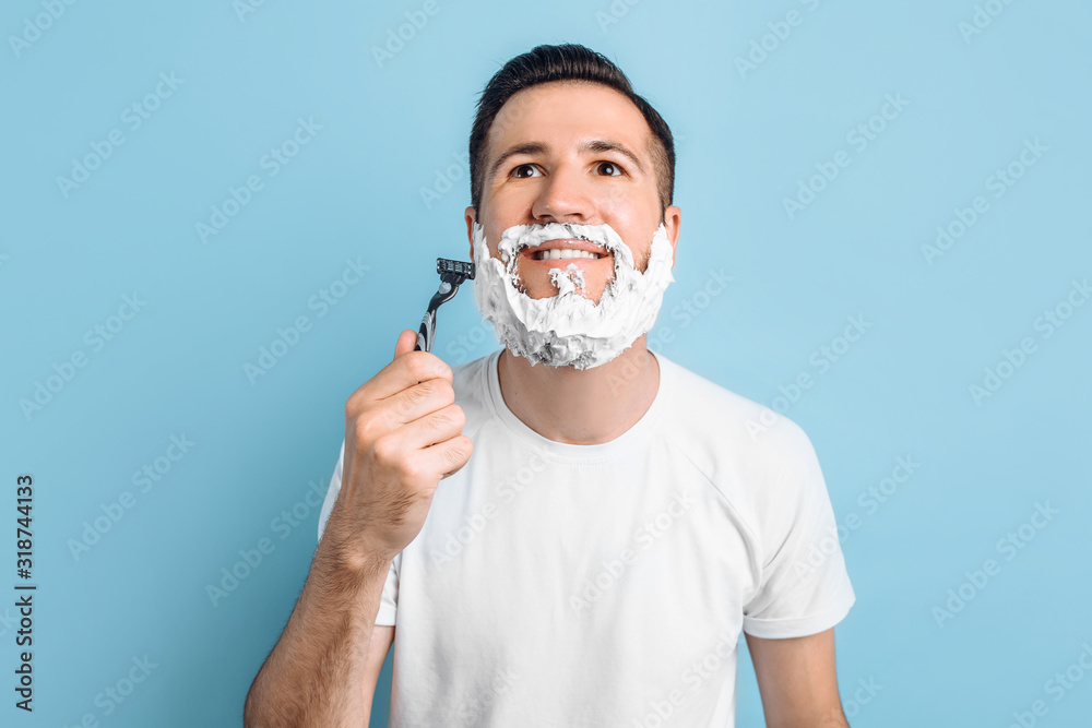 Positive young man with a beard shaves