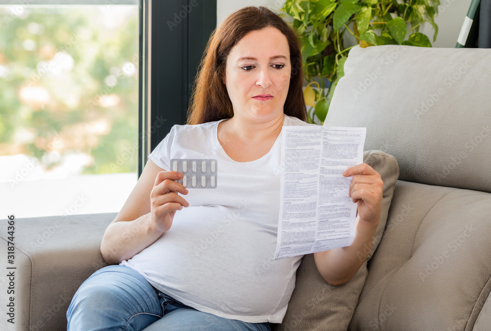 confused pregnant woman reading a leaflet before take a pill