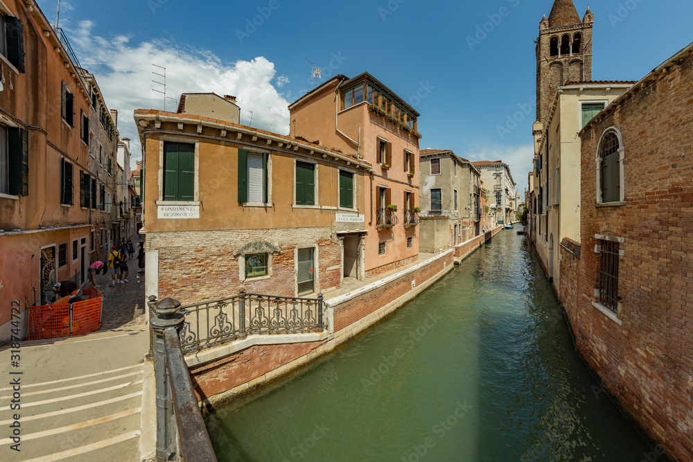 VENICE, ITALY - August 02, 2019: One of the thousands of lovely cozy corners in Venice on a clear sunny day. Locals and tourists strolling along the historical buildings and canals with moored boats