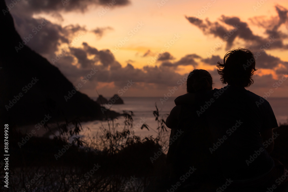 Silhouettes of people watching the sunset over the sea and the mountains.