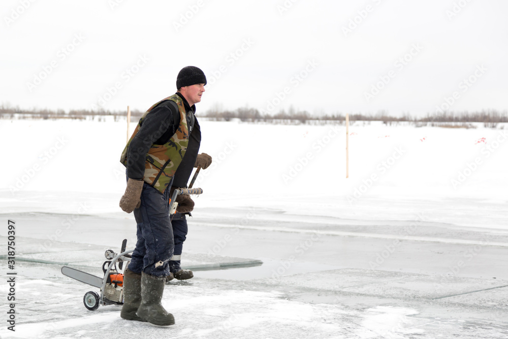 A worker walks on the ice of a frozen lake, with a sawing machine A worker walks on the ice of a frozen lake, with a sawing machine