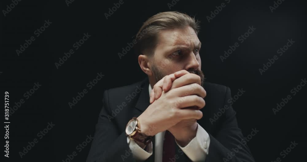 Masculine bearded man in formal suit waiting and rubbing hands in anxiety, isolated on black background Masculine bearded man in formal suit waiting and rubbing hands in anxiety, isolated on black background