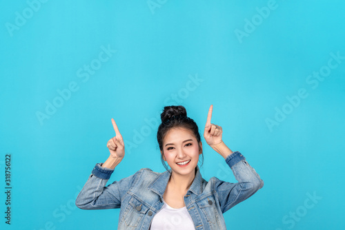 Obraz na plátně Happy asian woman feeling happiness and standing pointing hands up to copyspace on blue background