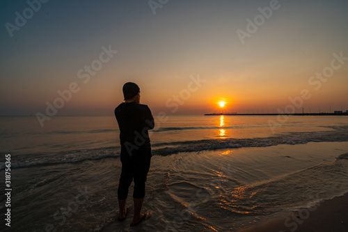 Unknown person watching sunset by the sea at a beach  during golden hour.