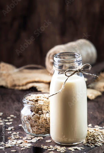 Vegan oat flakes milk, non dairy alternative milk in glass, wooden rustic table, copy space