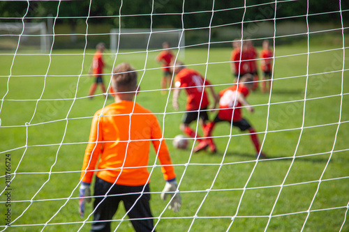 Goalkeeper catches the ball. Goal net in focus. Sports competition. Children's football on the field. Physical development. Children's sport. Sleight of hand. Ball Championship.