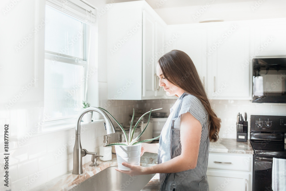Women holding indoor plant in a white kitchen Women holding indoor plant in a white kitchen