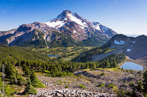 A high elevation volcanic peak seen in daylight in the summer with little snow and ice remaining on the slopes above tree line. photo