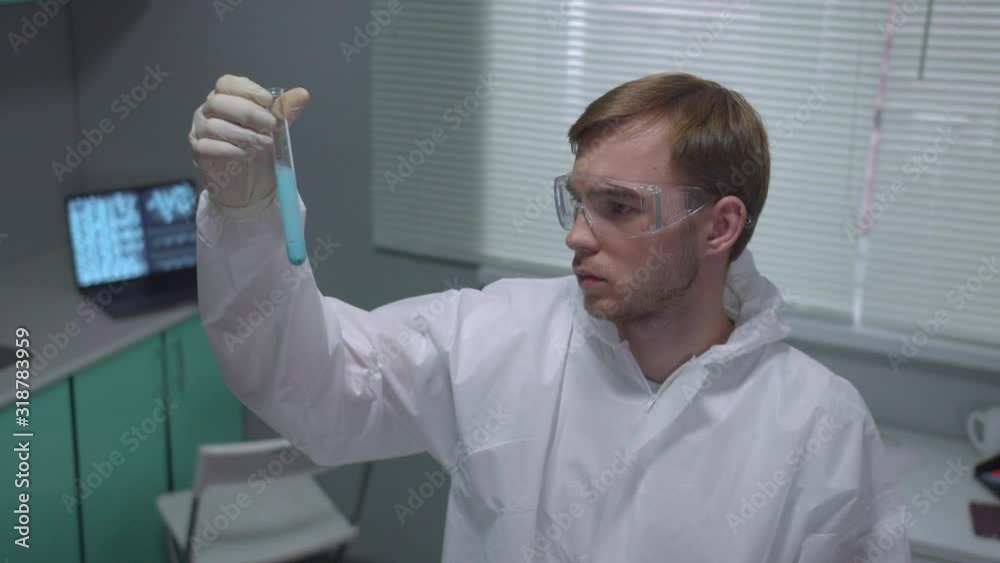 Chemist in protective workwear take tube with liquid and look seriously in the laboratory